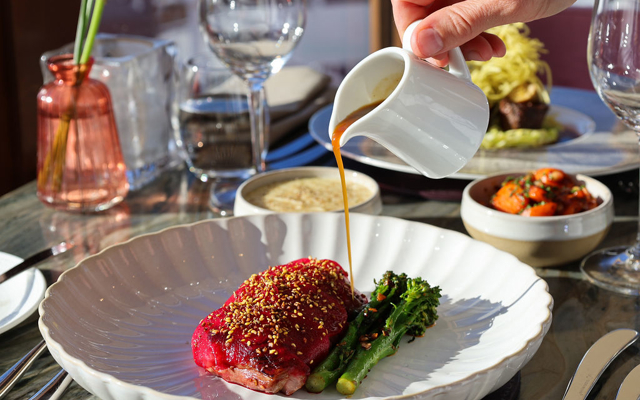 Roasted Devon duck breast on a white dish with the sauce being poured overtop 