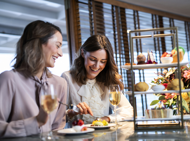 Two women enjoy afternoon tea in Edinburgh with 3 tier cake stand aboard Fingal's Lighthouse restaurant in Leith