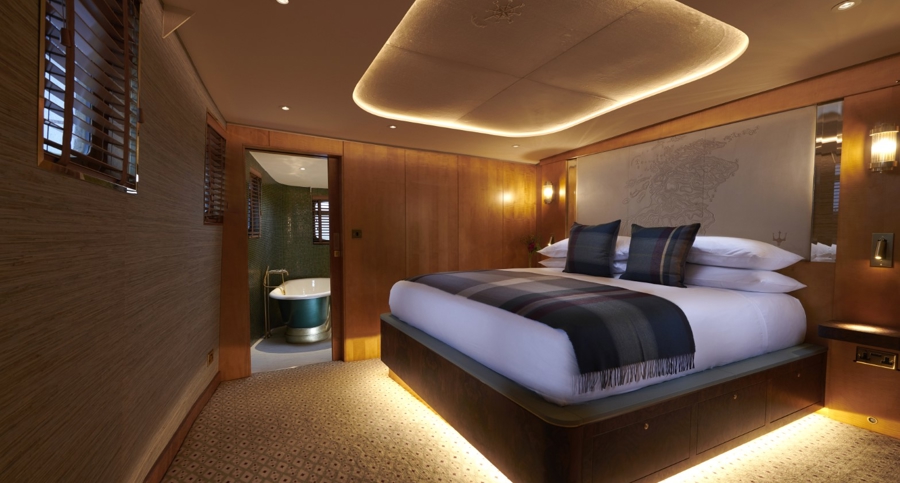 Skerryvore Hotel Suite aboard Fingal Hotel in Edinburgh featuring a super king-size bed with tartan accents, warm lighting, and an en-suite bathroom with elegant design.