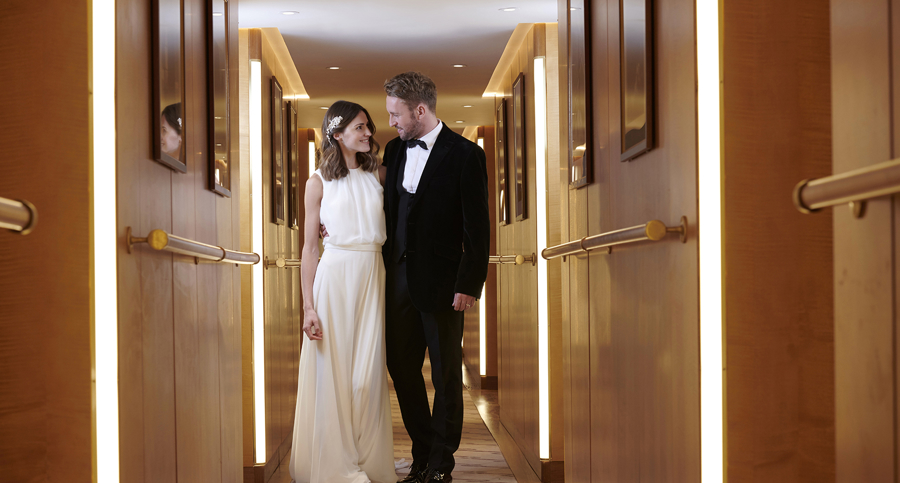 Bride and groom walking through the elegant hallway aboard Fingal Hotel in Edinburgh, representing a luxurious wedding or special occasion gift voucher experience.