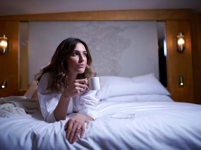 Guest relaxes with a cup of coffee on the bed in the Skerryvore Suite