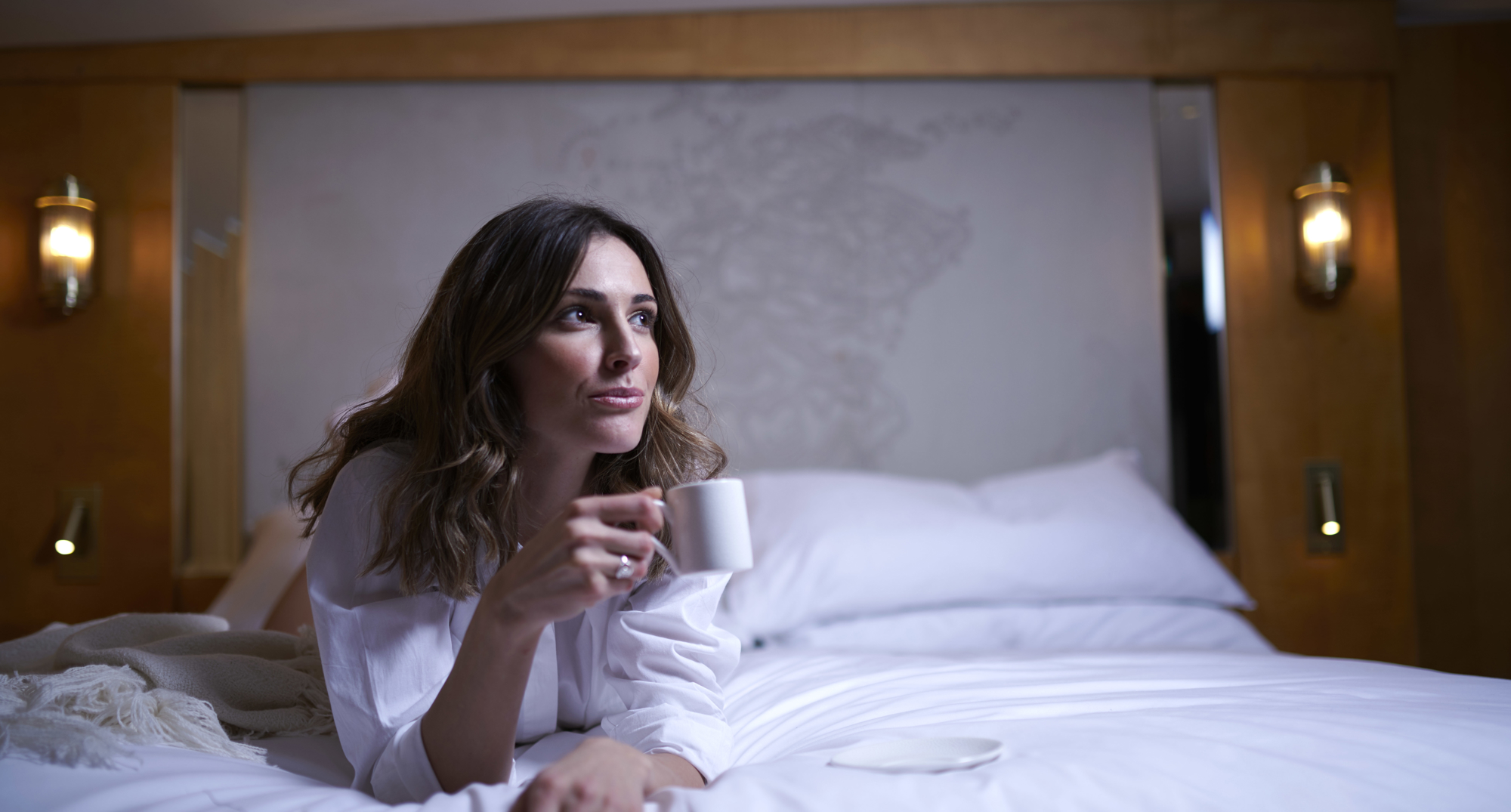 Woman on bed with up of coffee.
