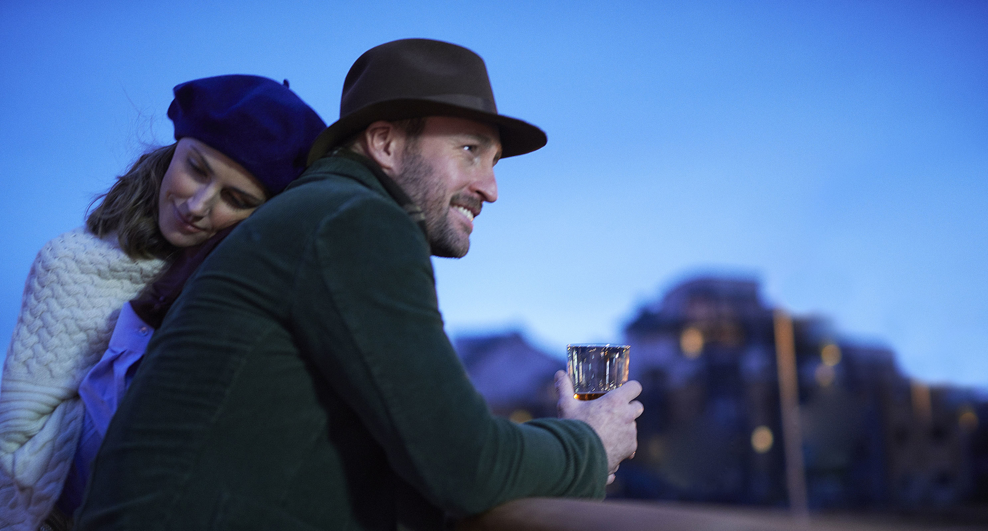 A couple lean over the railings with a glass of Whisky