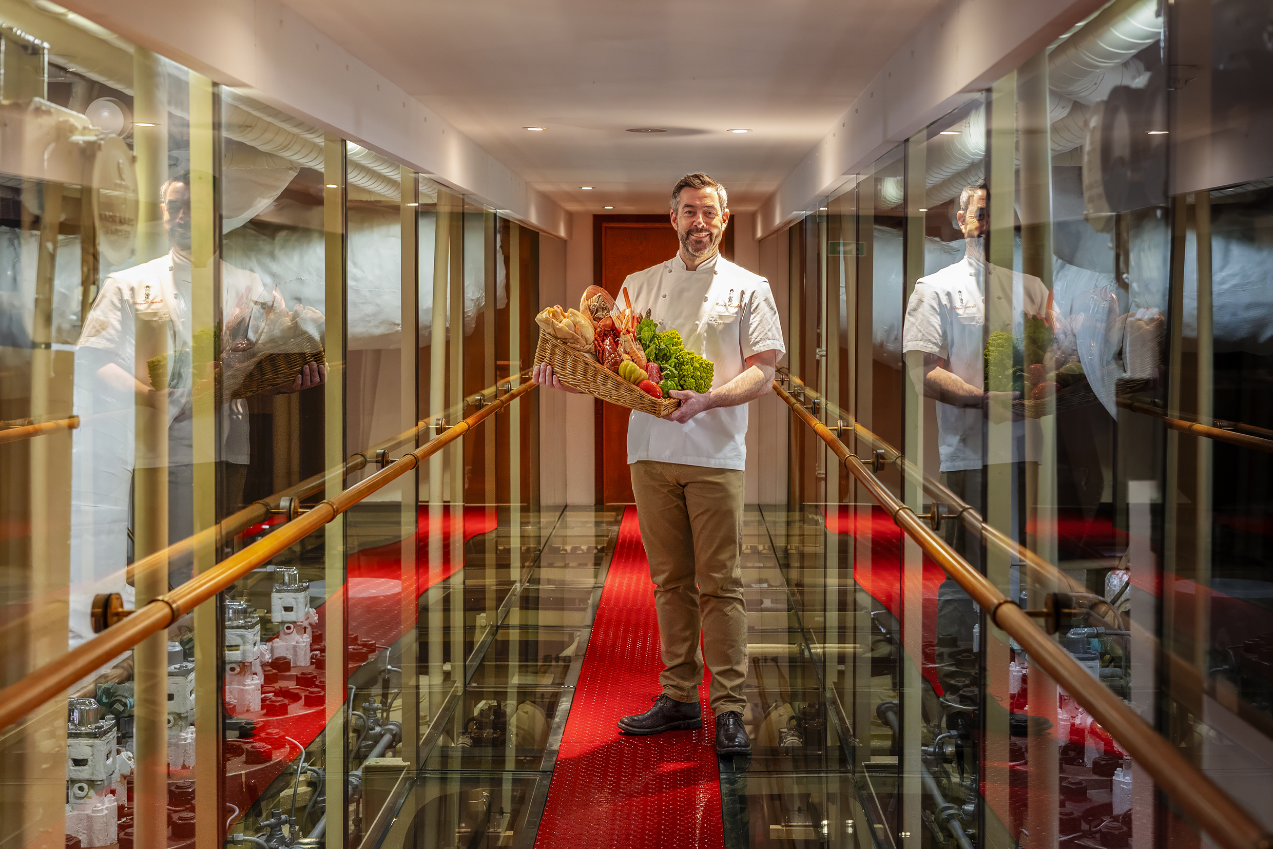 Chef holding fruit basket in an engine room on a ship.