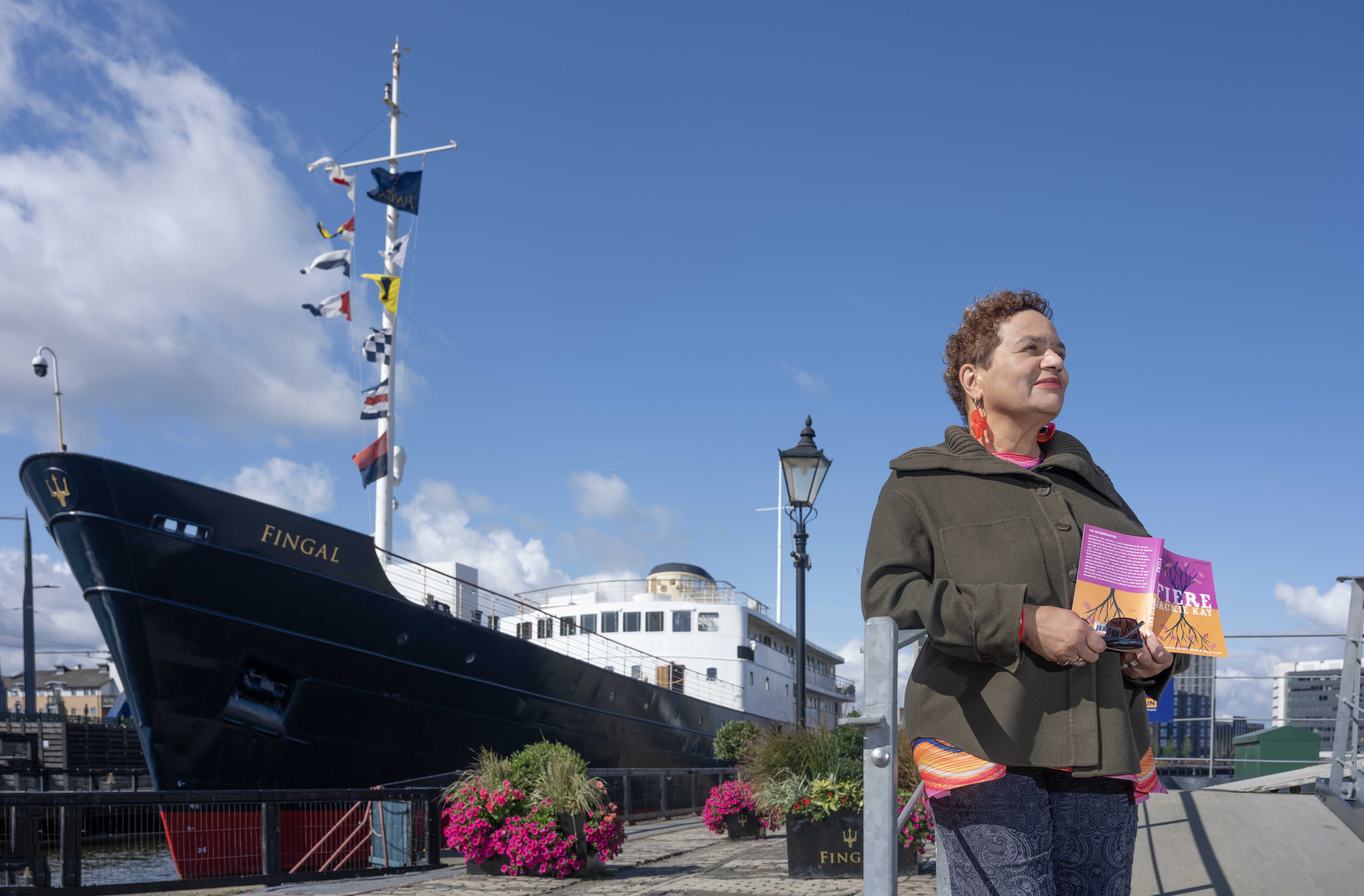 A woman with a book in her hand standing in front of a ship