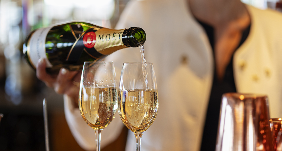 A hand pouring champagne into two glasses on a table.