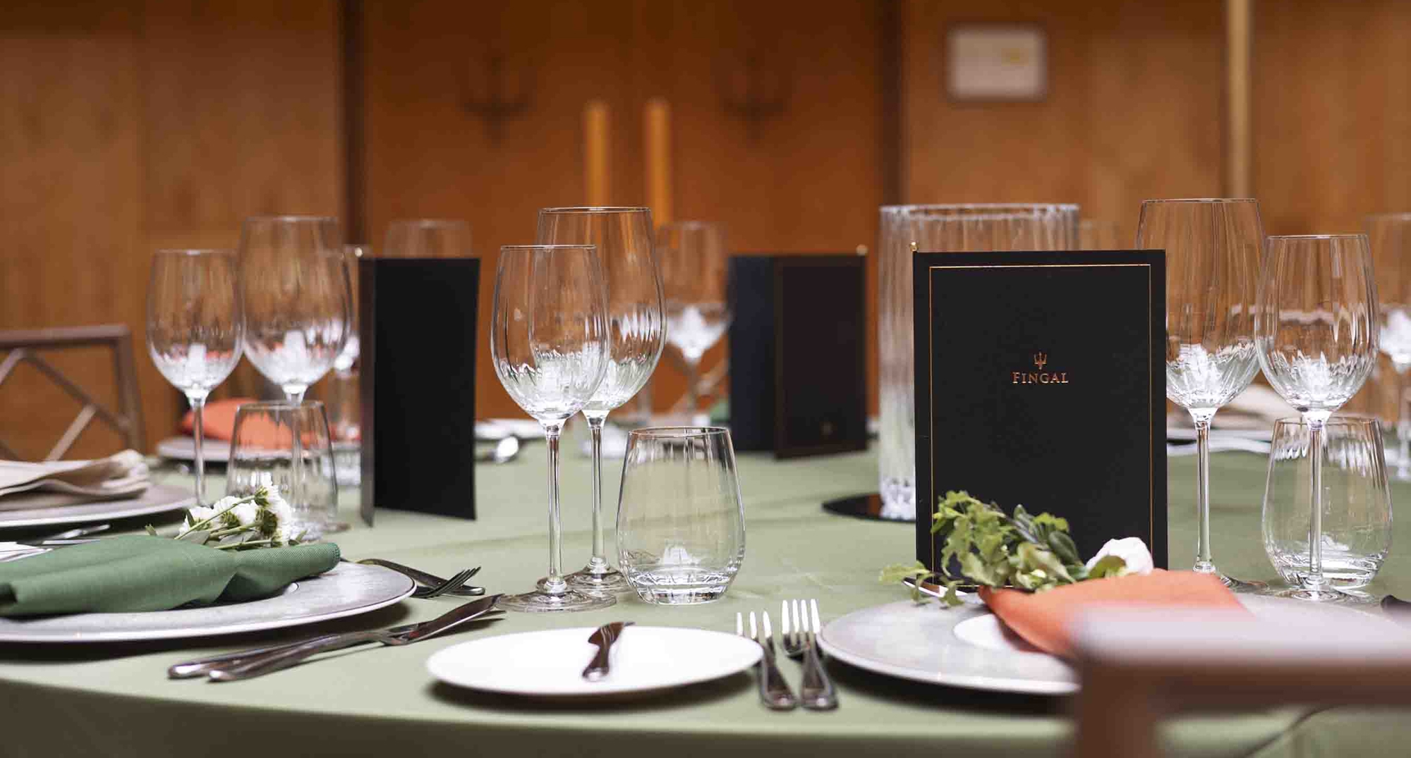 In the Ballroom, a table is set for an evening event with green tablecloth, silver cutlery, glasses and white dishes