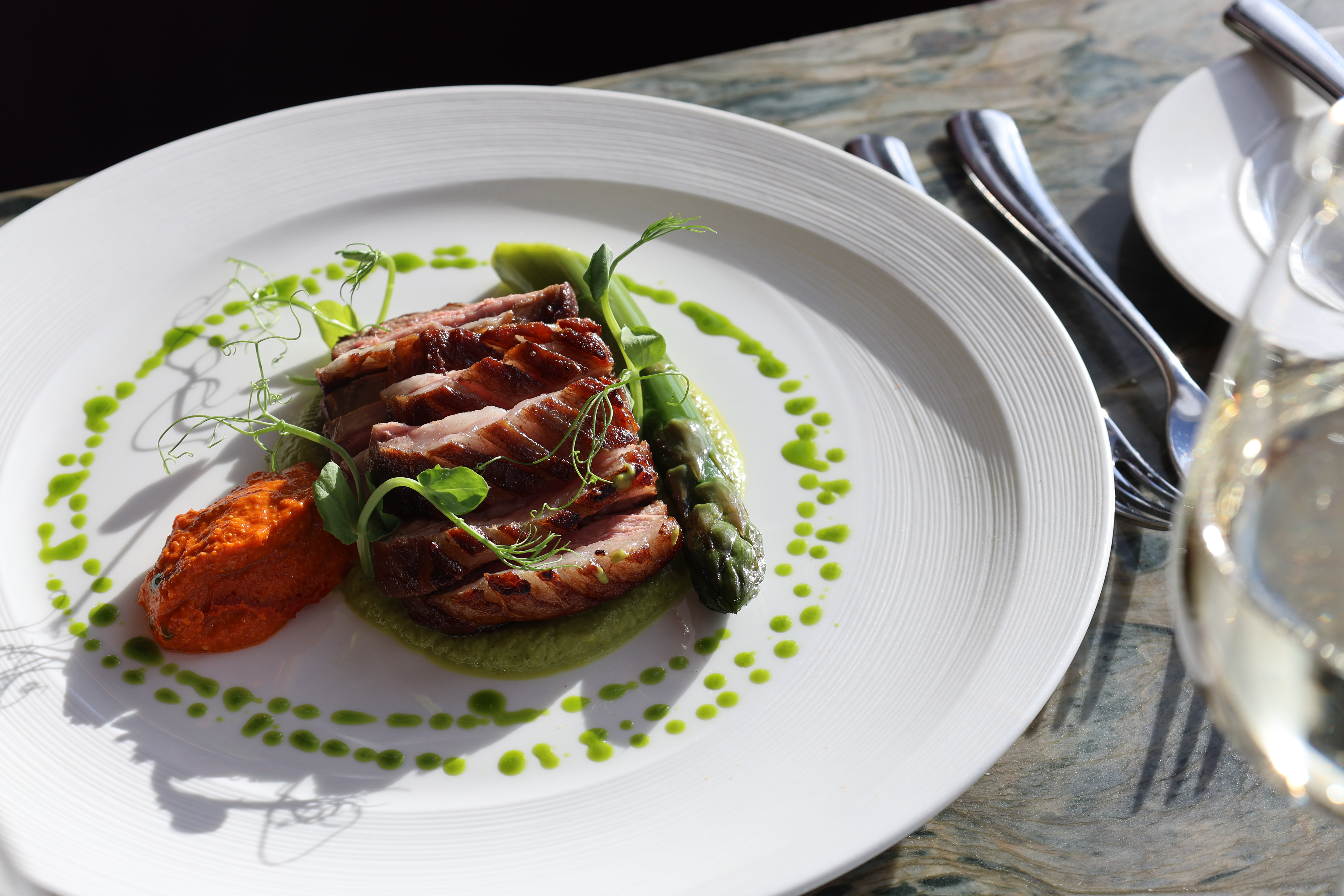 Tweed Valley lamb rump, courgette & basil purée,  romesco, asparagus & lamb jus on white plate