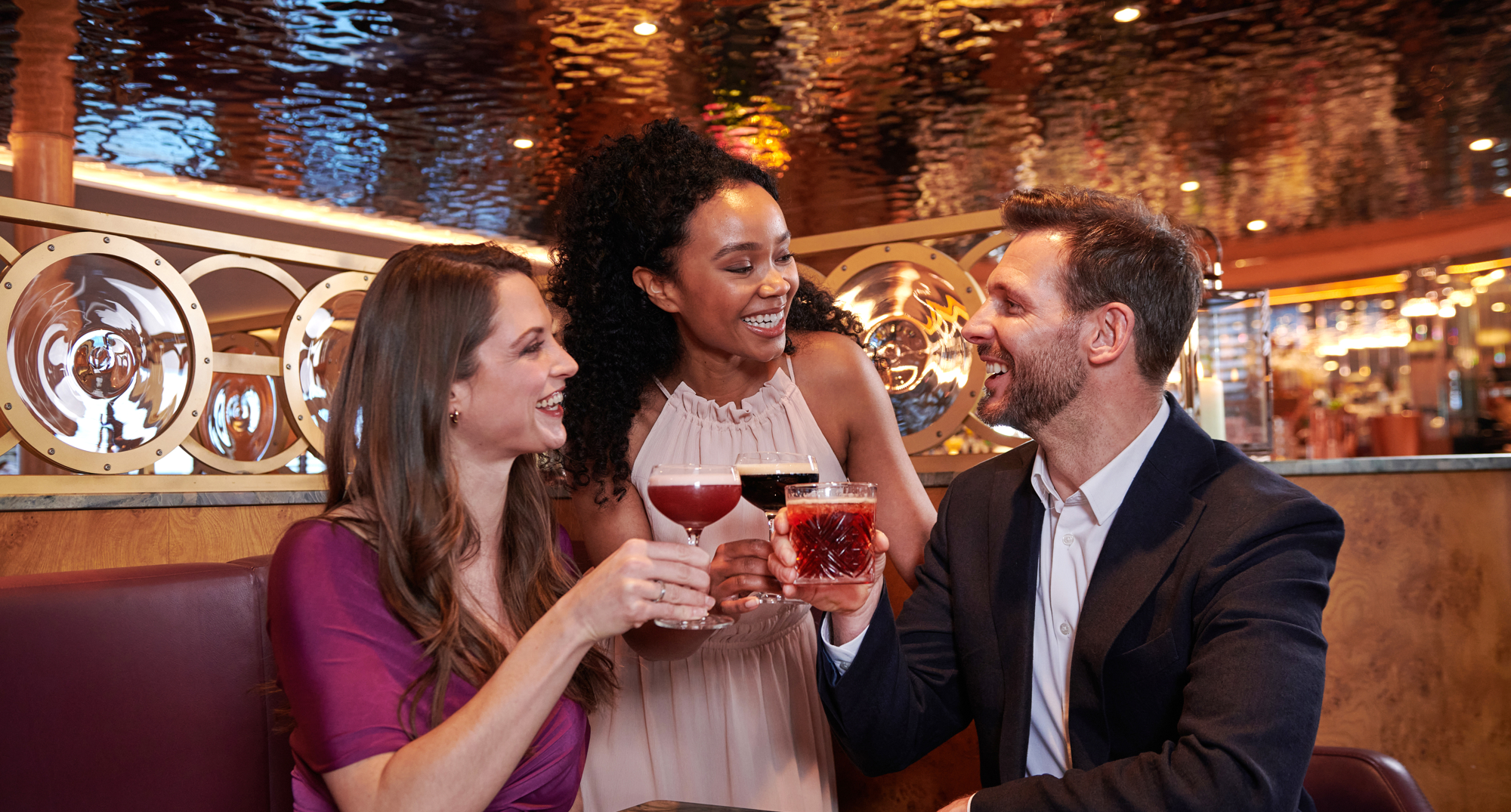 three people in a booth enjoying a cocktail