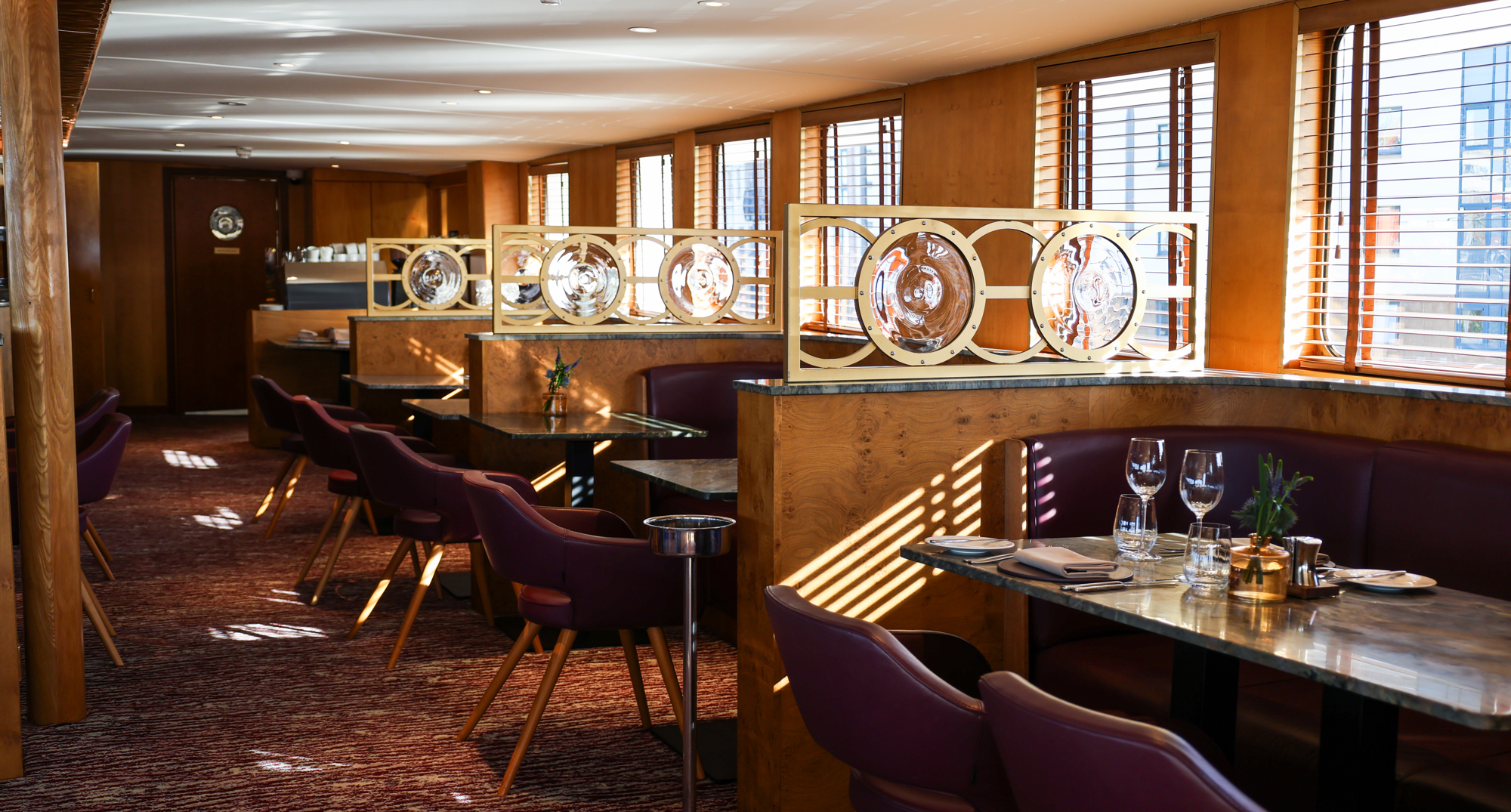 Interior shot of The Lighthouse restaurant aboard Fingal, an iconic floating hotel in Edinburgh, showcasing elegant tables set for fine dining with warm wood interiors, plush seating, and natural light streaming through the windows.