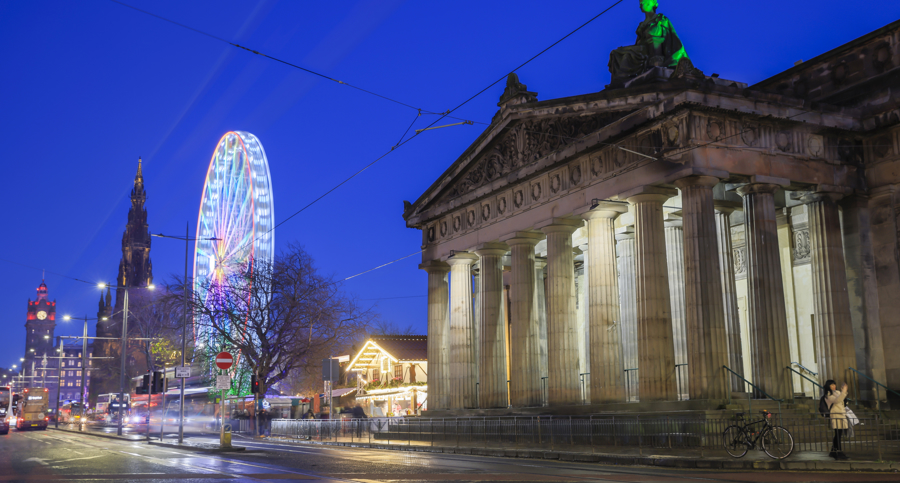 The National Galleries of Scotland on the Mound in Edinburgh in the evening during Christmas time. There is a giant illuminated wheel in the background. 