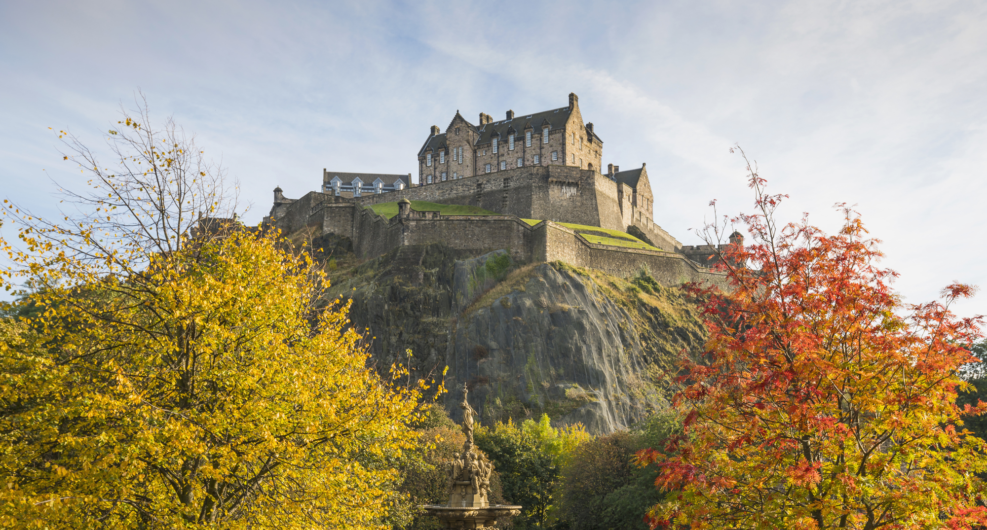Edinburgh Castle in the Autumn. There are golden and russet coloured trees in the foreground. 