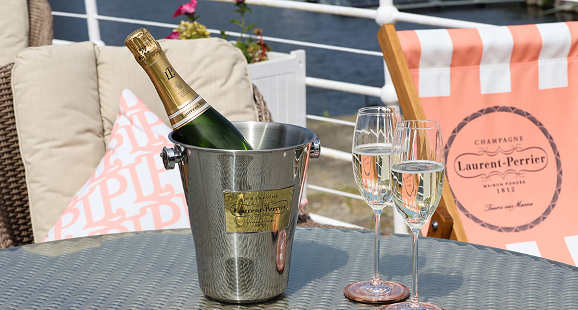 A silver ice bucket containing a bottle of Champagne and two glass flutes on a table on The Fingal Deck. 