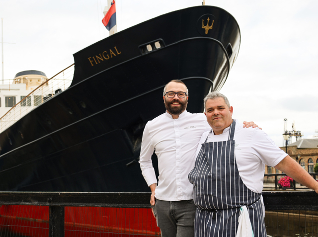 Dan and Pedro two men standing in front of a ship.