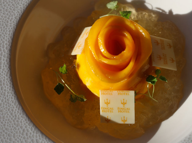 Orange mango dessert in the shape of a rose on a dish in the sunshine