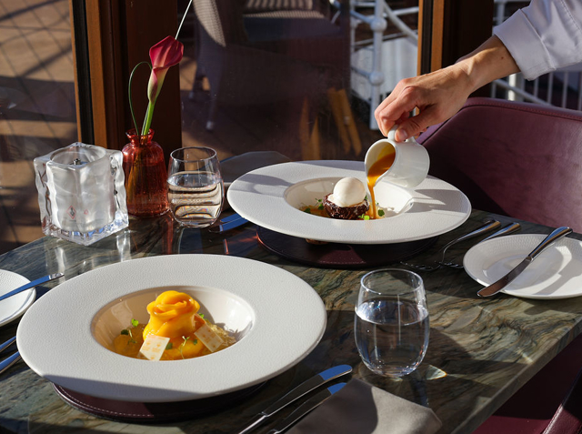 Desserts on a dining room table with sunshine coming through the windows and a chef pouring on a sweet sauce