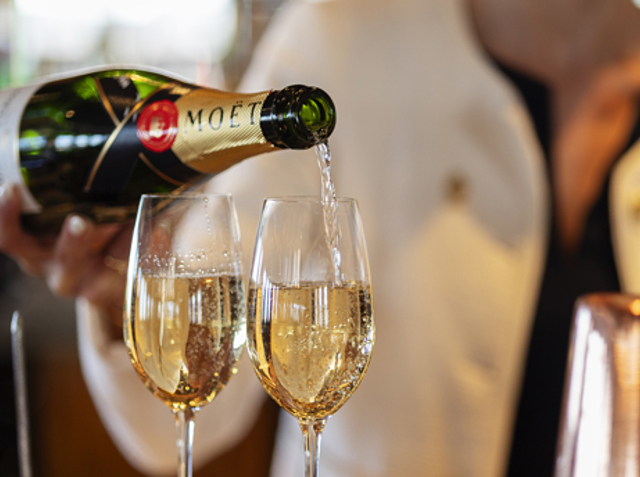 A woman is pouring a glass of Champagne in Fingal Hotel's Lighthouse Restaurant.