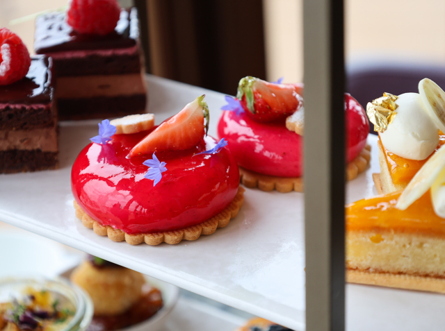 Assortment of colourful patisserie desserts on a tiered stand, including red domes, chocolate slices, and citrus‑glazed cakes.