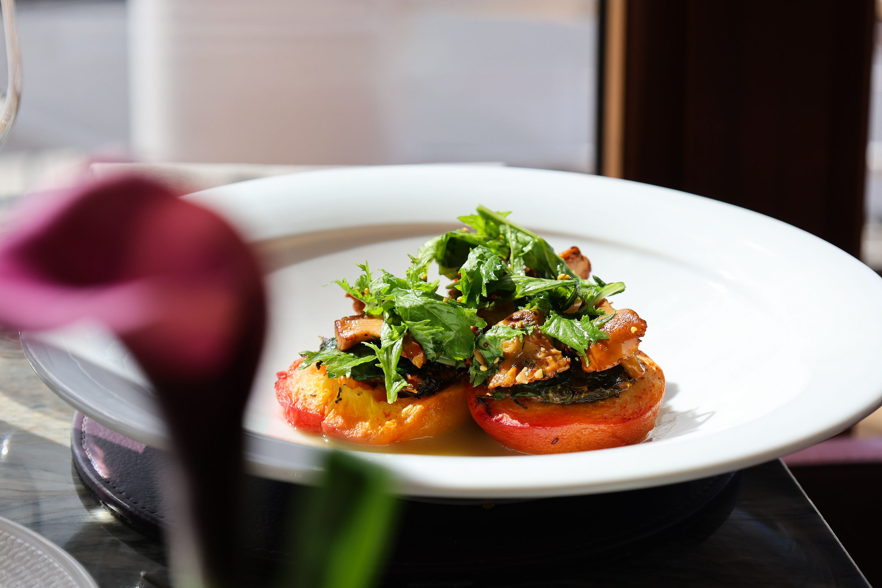 Roast peach topped with nasturtium, roquette and foraged Scottish mushrooms, arranged on a white plate with soft natural light and a blurred pink flower in the foreground.
