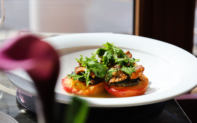 Roast peach topped with nasturtium, roquette and foraged Scottish mushrooms, arranged on a white plate with soft natural light and a blurred pink flower in the foreground.