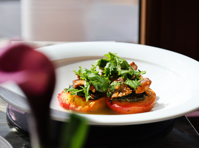 Roast peach topped with nasturtium, roquette and foraged Scottish mushrooms, arranged on a white plate with soft natural light and a blurred pink flower in the foreground.