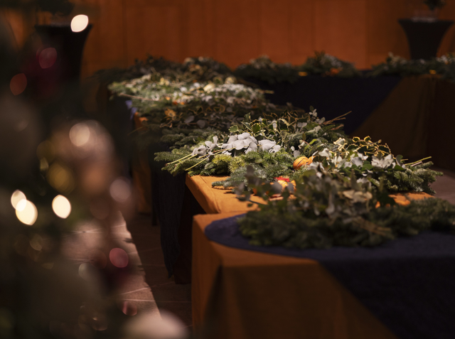 A warmly lit room with tables decorated with evergreens, pine branches, and citrus accents for a holiday workshop.