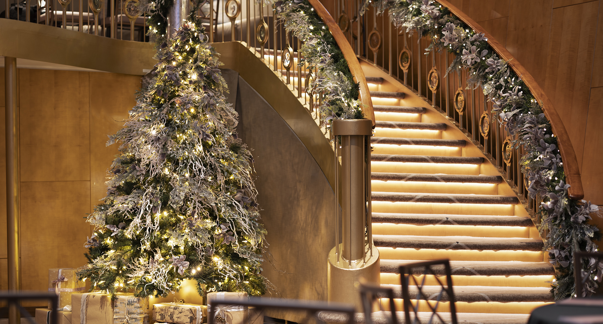 A Christmas tree next to a sweeping staircase in Fingal's Ballroom. There is a garland around the staircase bannister. 